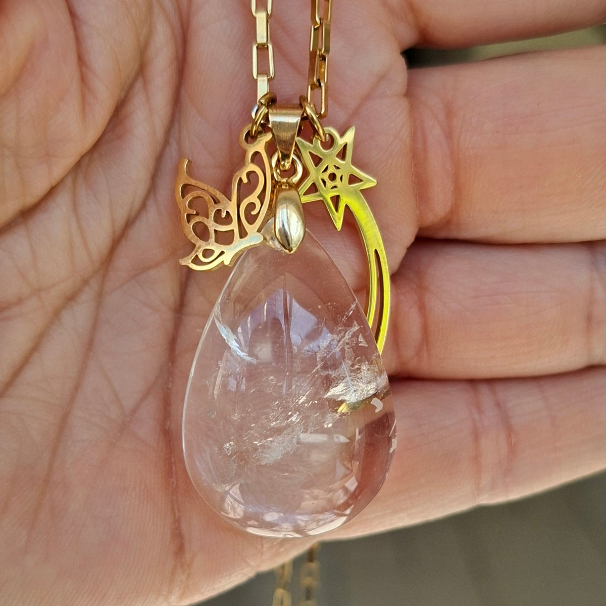 Collier cristal de roche naturel forme goutte et acier inoxydable doré dans la main