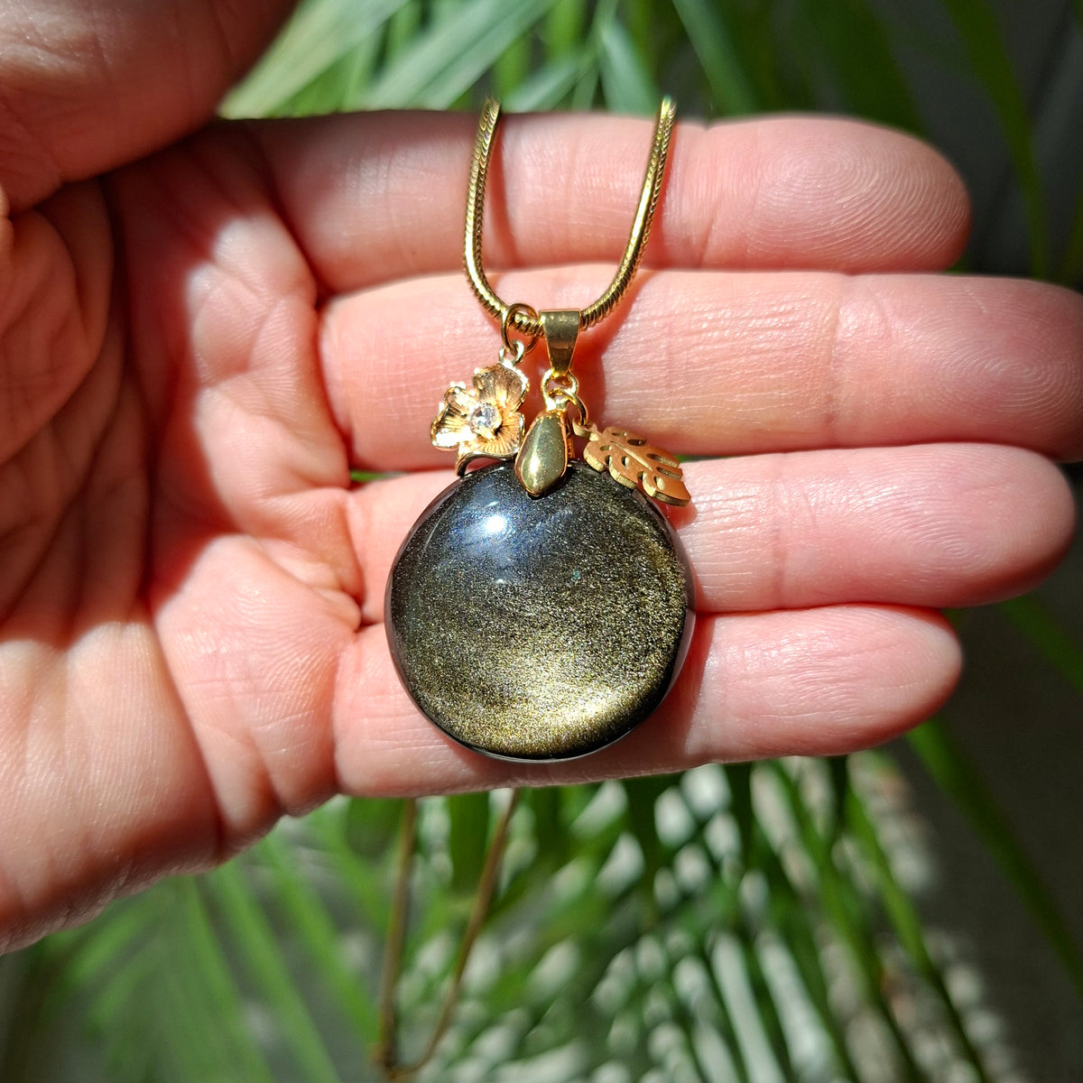 Collier en obsidienne dorée ronde avec breloques et chaîne acier dans la main