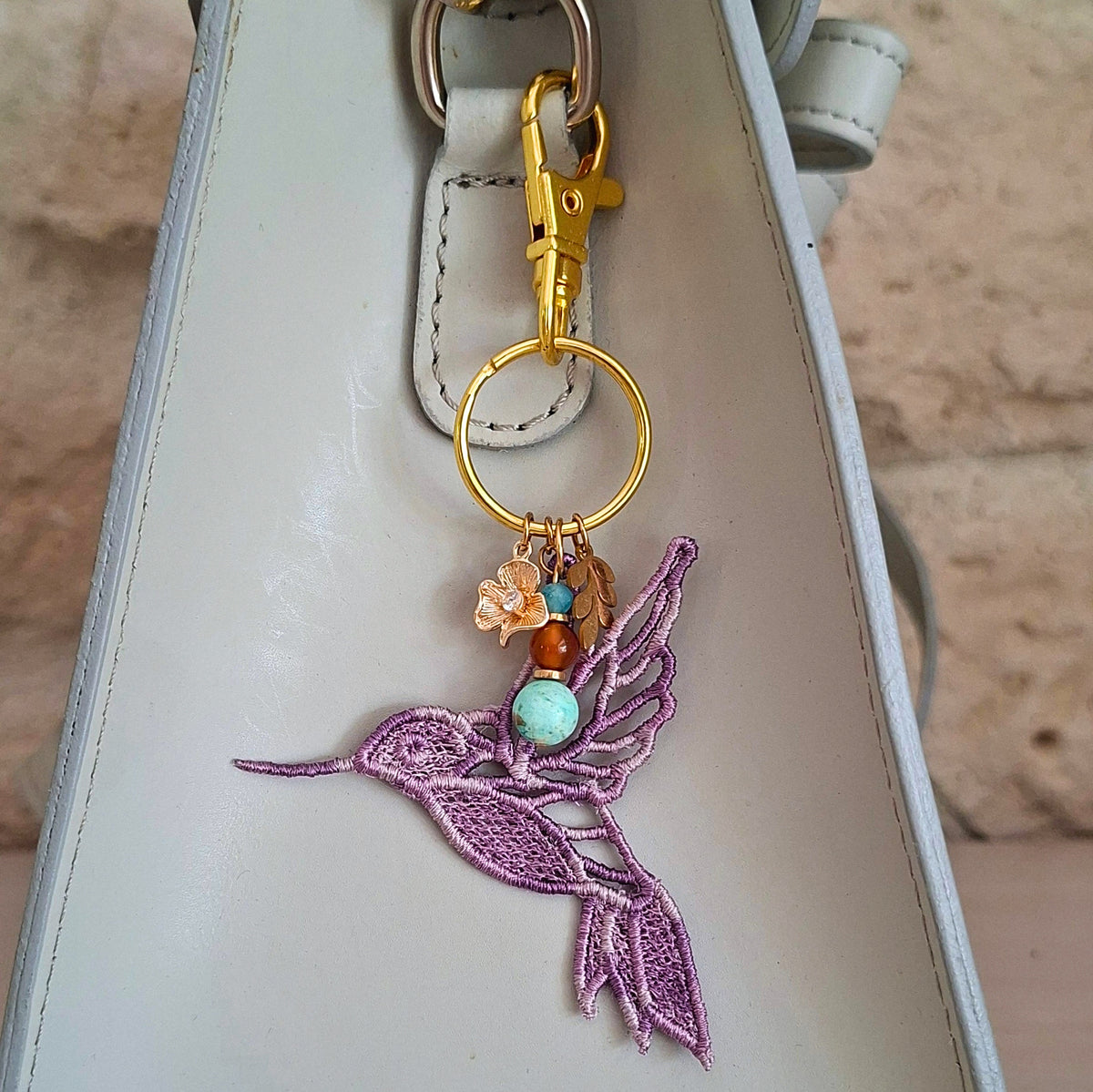 Bijou de sac Colibri Joie de vivre mauve porté sur un sac avec pierres naturelles et détails dorés