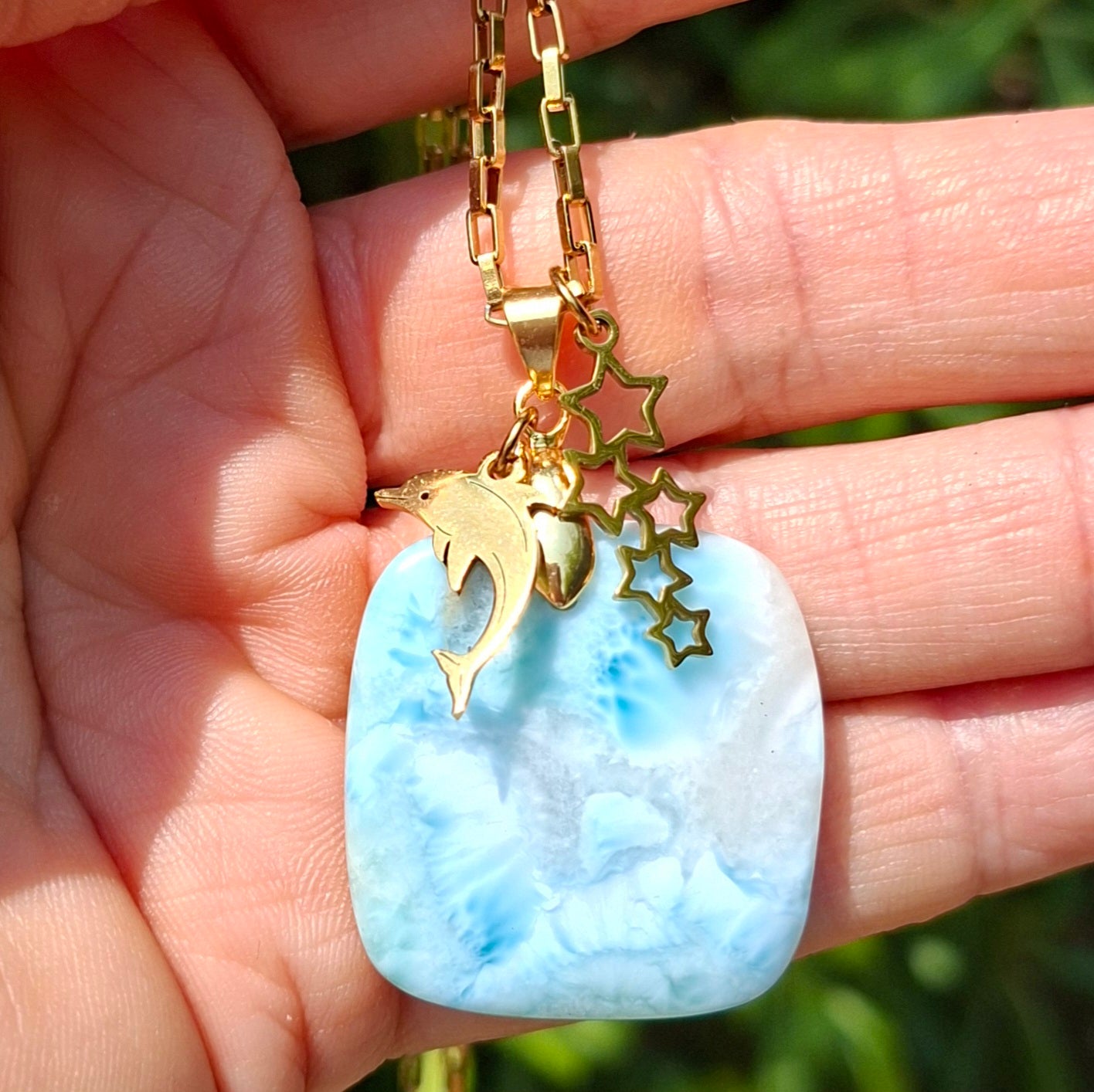 Collier asymétrique en larimar carré présenté dans la main avec breloques dorées