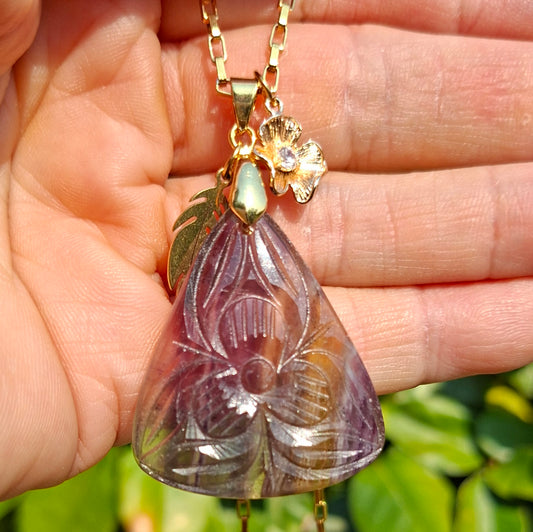 Collier en fluorite ciselée tenu dans la main montrant les nuances violettes de la pierre