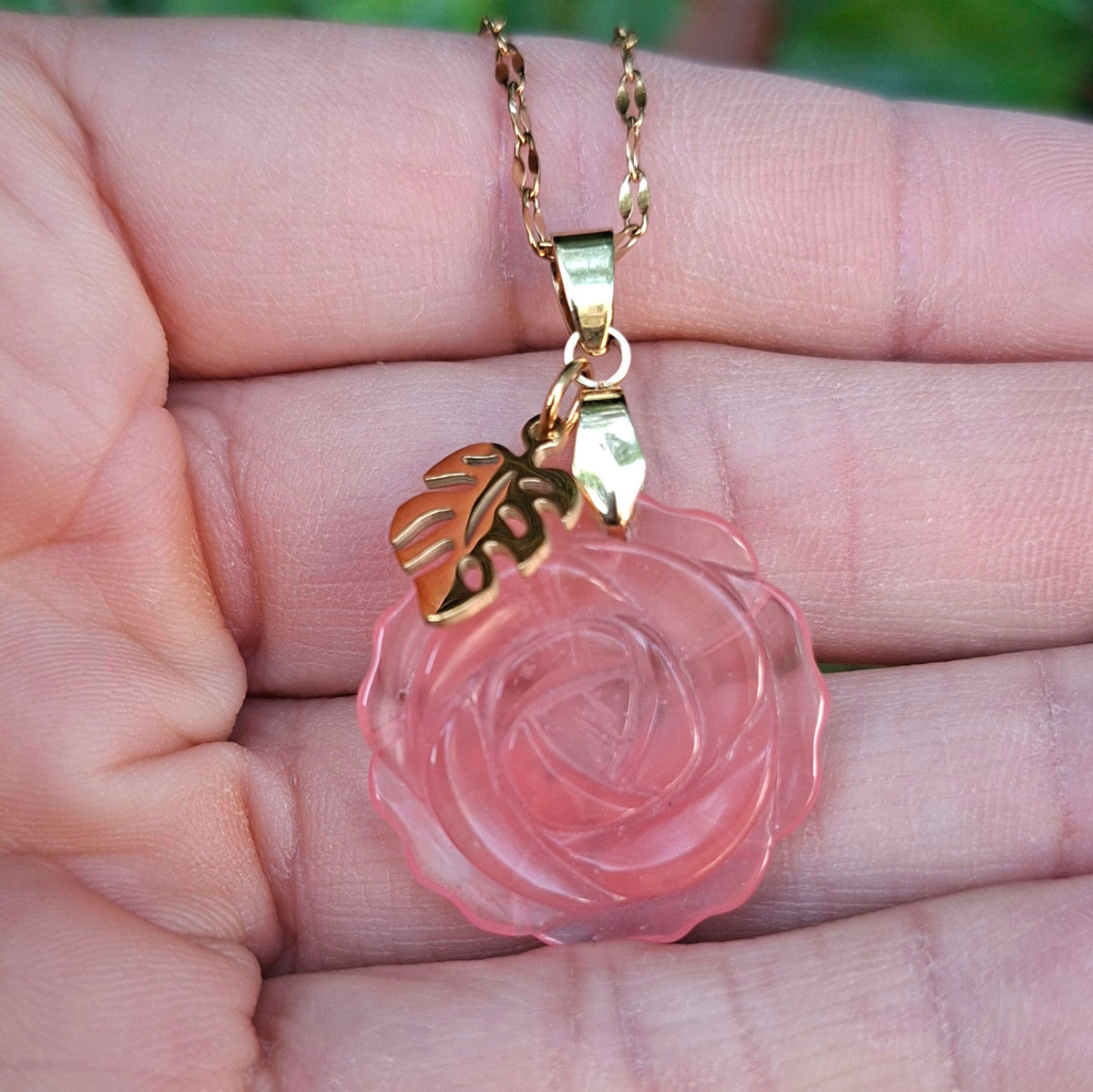 Collier en tourmaline melon d'eau rose sculptée en forme de rose présenté dans la main.