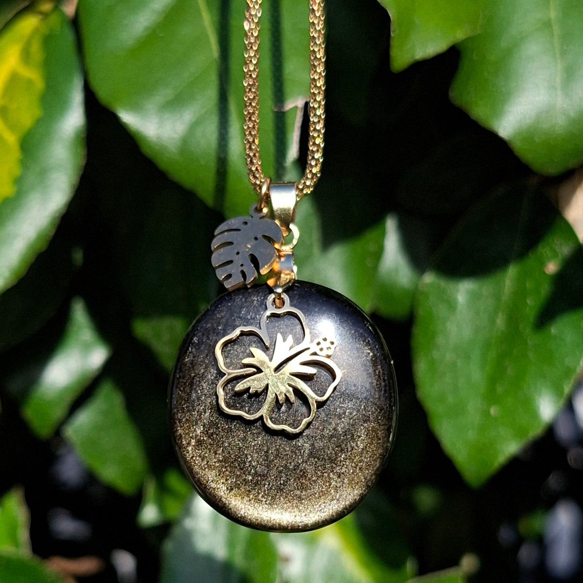 Collier en obsidienne dorée sur chaîne dorée maille bambou avec breloques hibiscus et feuille de monstera.