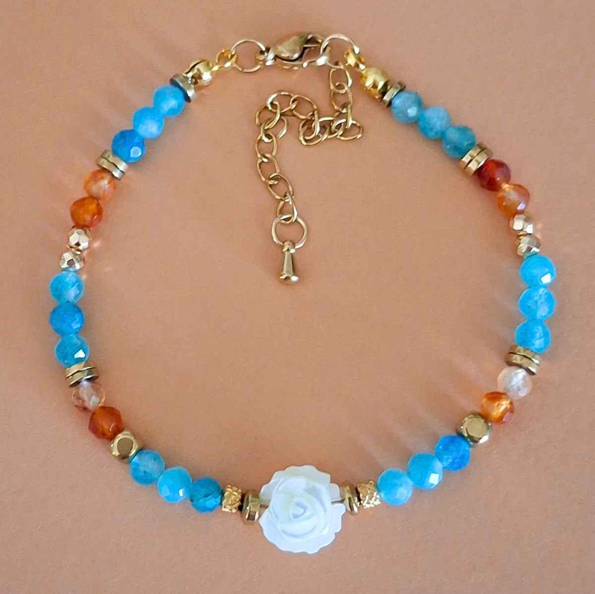 Bracelet Célia en perles facettées d'apatite bleue et de cornaline orange, avec rose centrale en nacre et finitions dorées