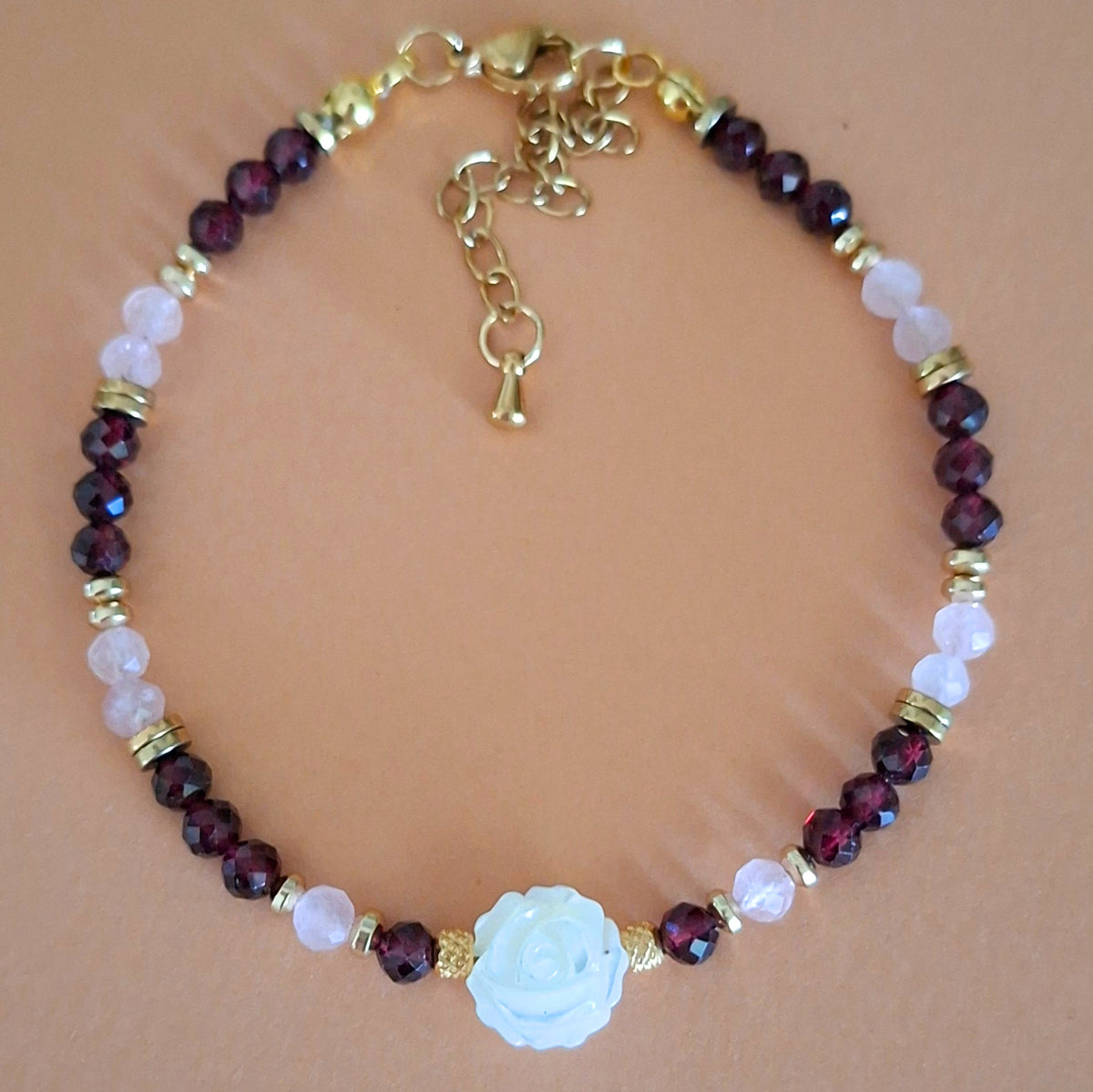 Bracelet Célia en perles facettées de grenat et quartz rose, avec rose centrale en nacre et finitions dorées