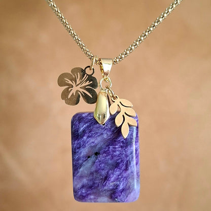 Collier en charoïte rectangulaire violette avec breloque feuille et fleur d'hibiscus dorées.