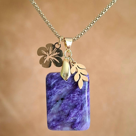 Collier en charoïte rectangulaire violette avec breloque feuille et fleur d'hibiscus dorées.