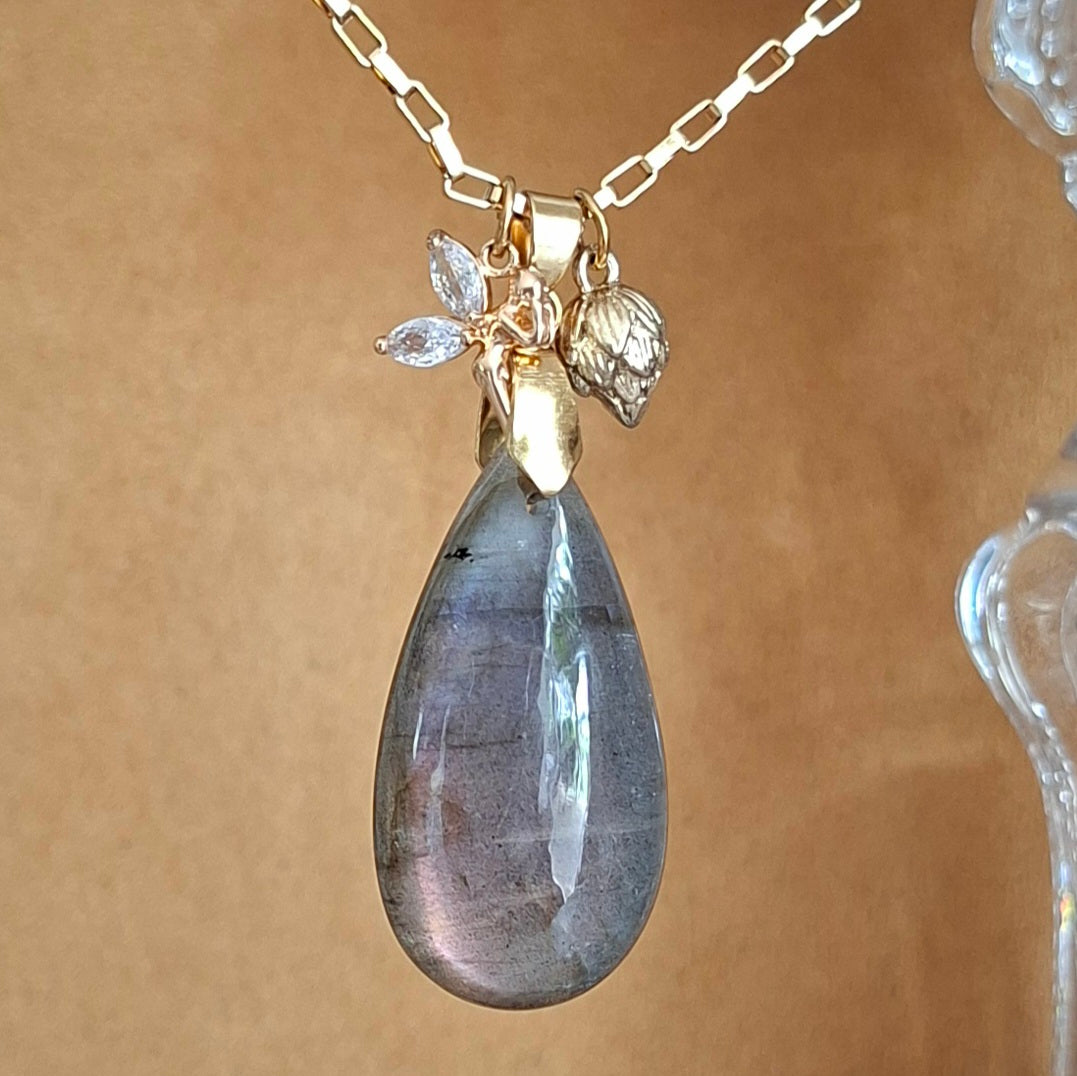 Collier en labradorite violette en forme de goutte avec breloques fée et bouton de lotus en acier doré. 