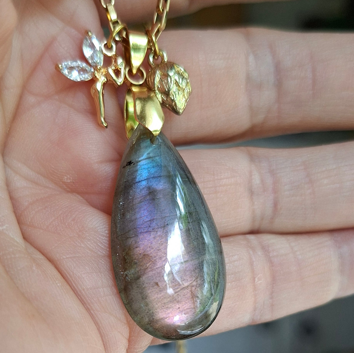 Collier en labradorite violette en forme de goutte avec breloques fée et bouton de lotus en acier inoxydable dans la main
