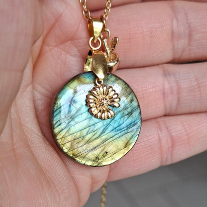 Collier acier doré en labradorite ronde présenté dans la main avec breloques fleur et pomme dorée.