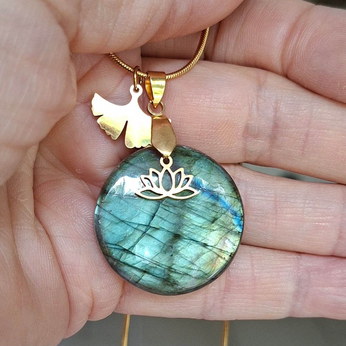 Collier en labradorite ronde avec breloques fleur de lotus et feuille de ginkgo en acier inoxydable doré dans la main.