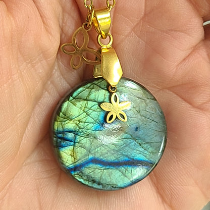 Collier acier doré en labradorite ronde aux reflets multicolores avec breloques fleur et papillon dans une main - Petite Rainette Bijoux