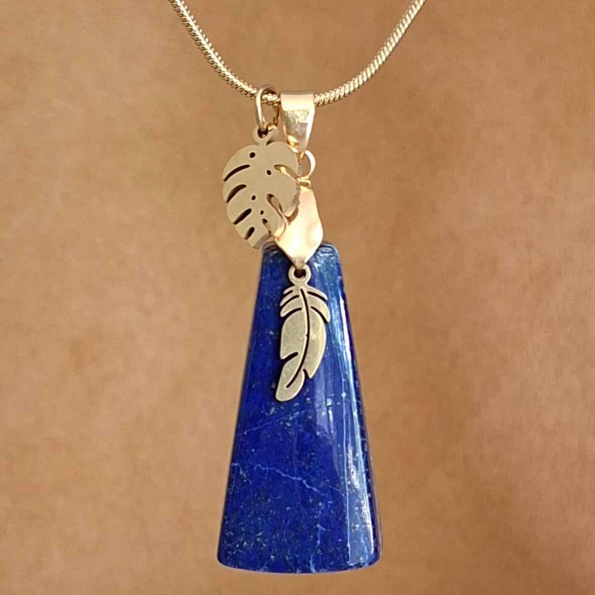 Collier en lapis-lazuli triangulaire avec breloques plume et feuille en acier doré.