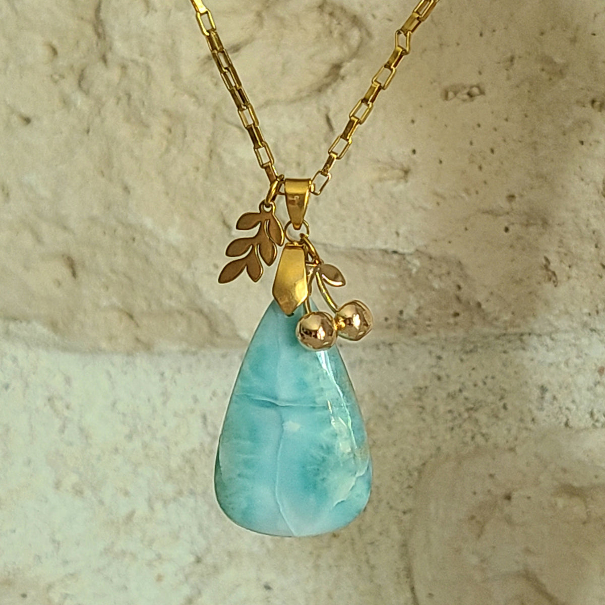 Collier en larimar bleu clair taillé en forme de poire avec breloques feuille et cerises sur chaîne dorée.