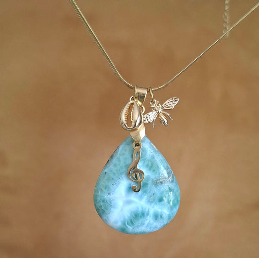 Collier en larimar bleu clair taillé en forme de poire avec breloques clé de sol, abeille et coquillage sur chaîne dorée.