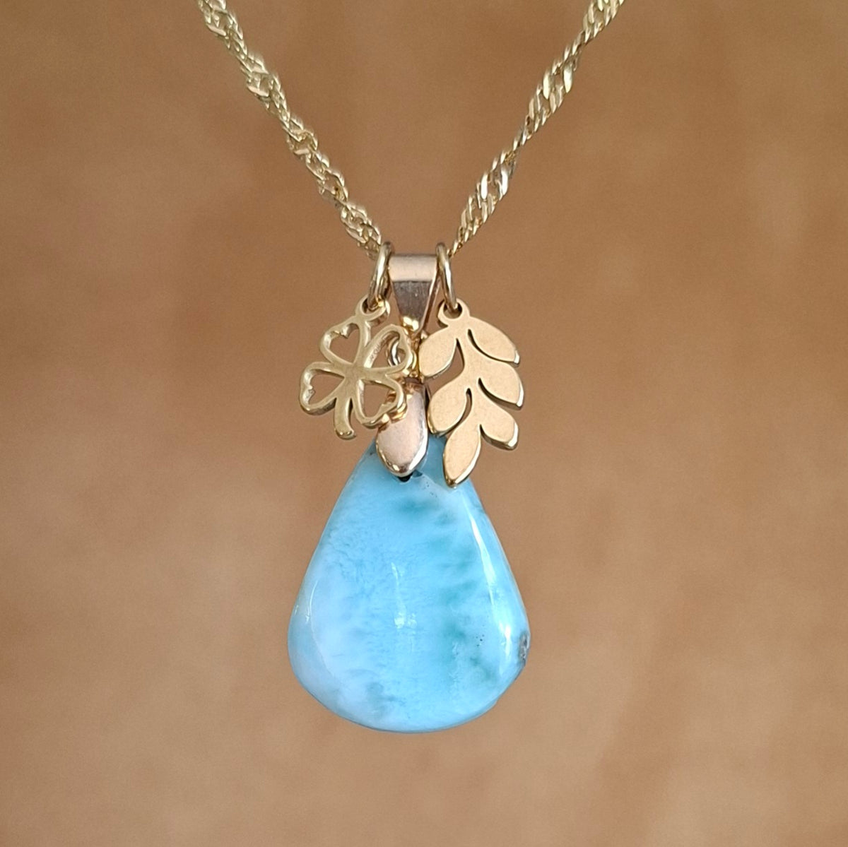 Collier en acier inoxydable doré avec larimar bleu taillé en poire, breloques feuille et trèfle.