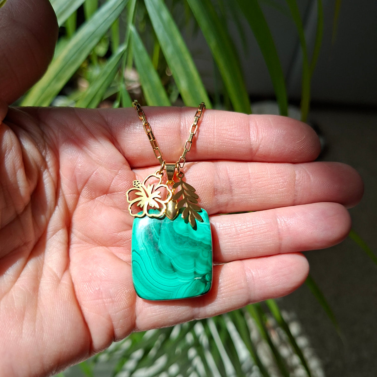 Collier malachite rectangulaire et chaîne acier doré avec breloques dans la main