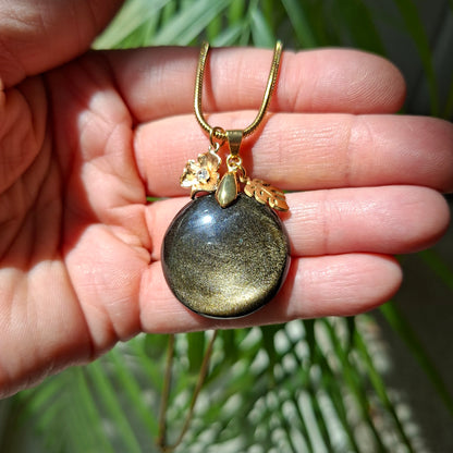 Collier en obsidienne dorée ronde avec breloques et chaîne acier dans la main