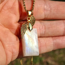 Charger l'image dans la galerie, Collier artisanal en pierre de lune arc-en-ciel labradorite blanche dans la main, avec reflets bleus et breloques dorées
