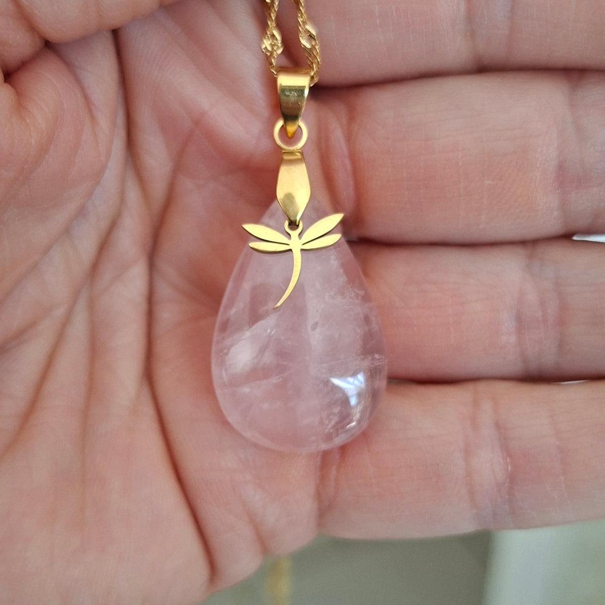 Collier quartz rose forme goutte sur chaine acier doré dans la main