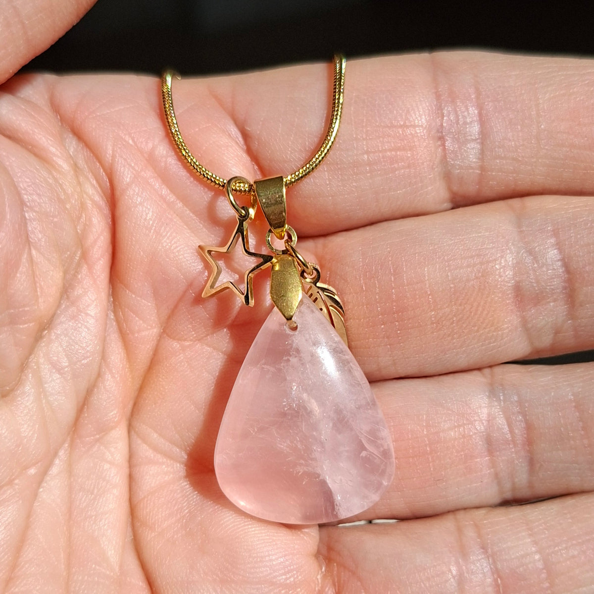 Collier en quartz rose naturel forme goutte sur chaîne acier inoxydable doré avec breloques étoile et plume dans la main