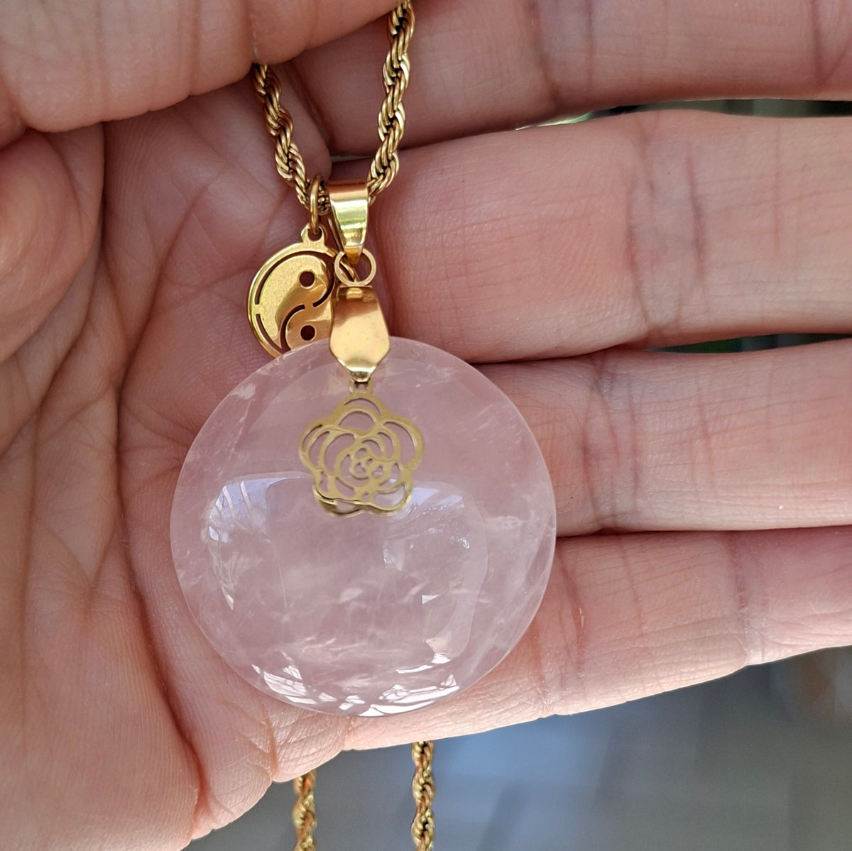 Collier en quartz rose naturel rond sur chaîne acier inoxydable doré avec breloques fleur et yin yang dans la main