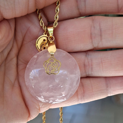Collier en quartz rose naturel rond sur chaîne acier inoxydable doré avec breloques fleur et yin yang dans la main