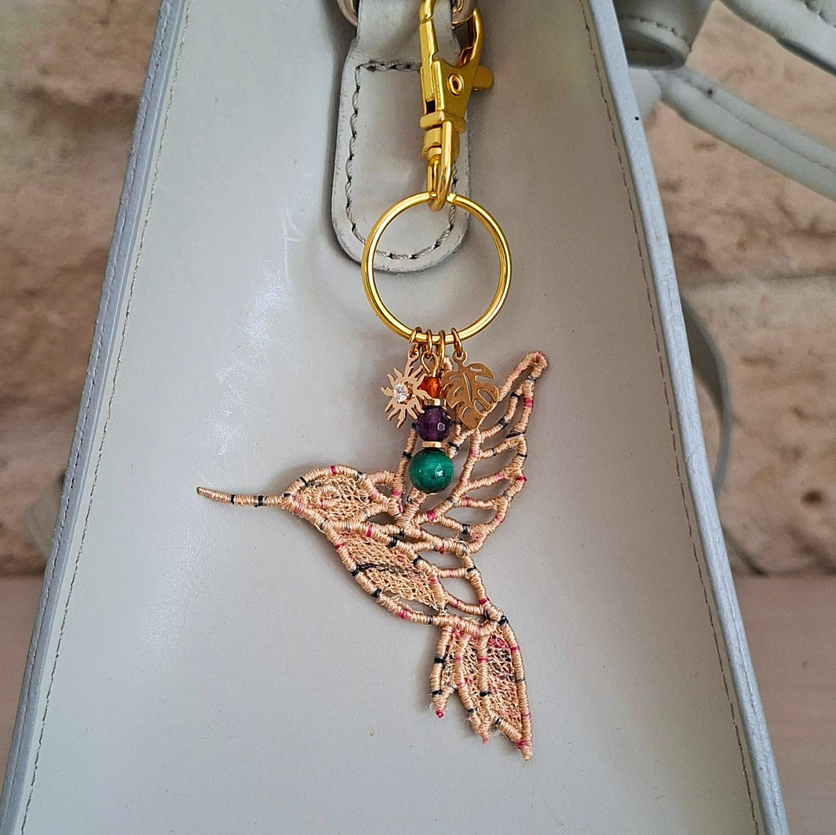 Bijou de sac Colibri Joie de vivre beige porté sur un sac avec pierres naturelles et détails dorés
