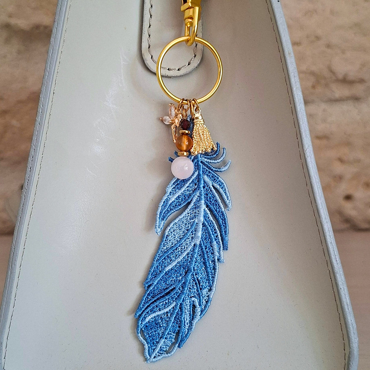 Bijou de sac Plume Liberté bleue porté sur un sac avec pierres naturelles et détails dorés
