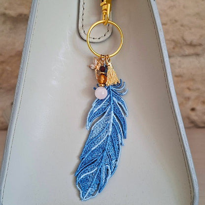 Bijou de sac Plume Liberté bleue porté sur un sac avec pierres naturelles et détails dorés