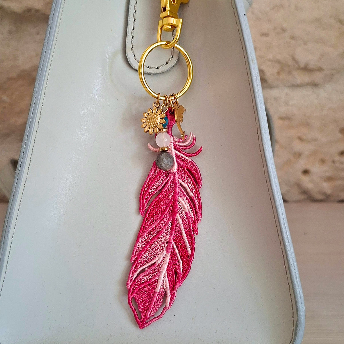 Bijou de sac Plume Liberté fuchsia portée sur un sac avec pierres naturelles et détails dorés