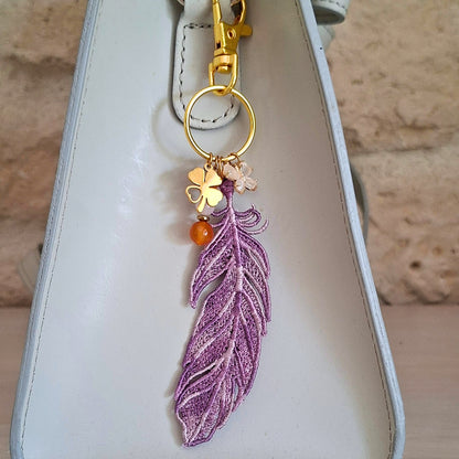 Bijou de sac Plume Liberté mauve portée sur un sac avec pierres naturelles et détails dorés