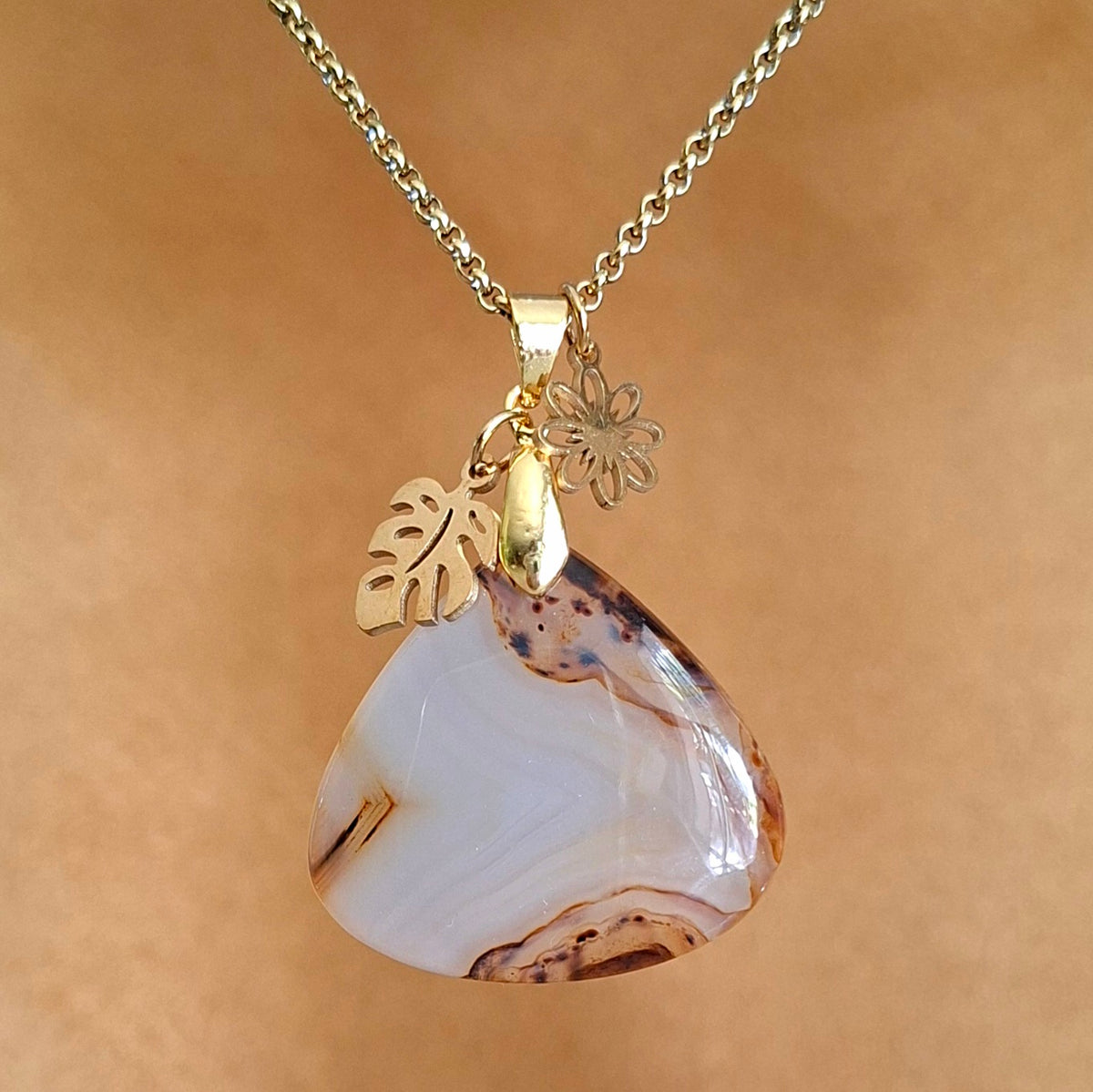 Collier en agate du Montana naturelle aux nuances crème et caramel avec breloques fleur et feuille dorées.