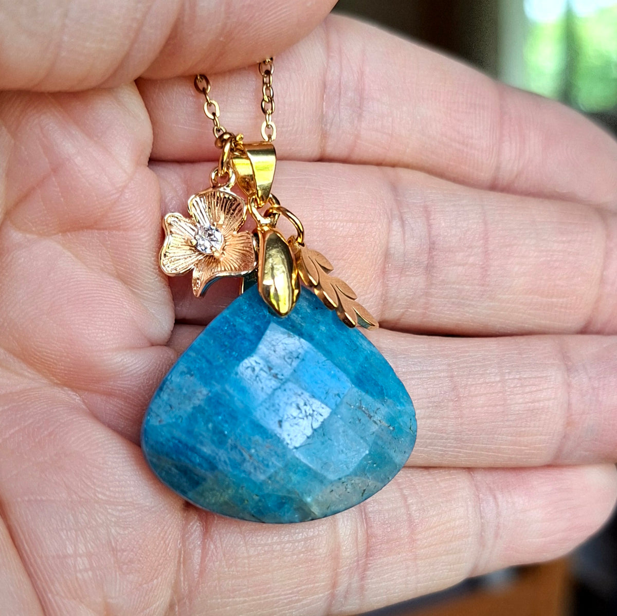 Collier en apatite triangulaire facettée présenté dans la main avec breloques fleur et feuille.