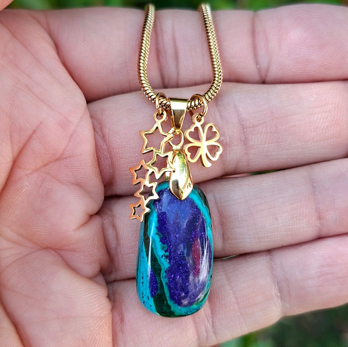 Collier en azurite naturelle bleue aux contrastes verts tenu dans la main, avec breloques étoiles et trèfle.