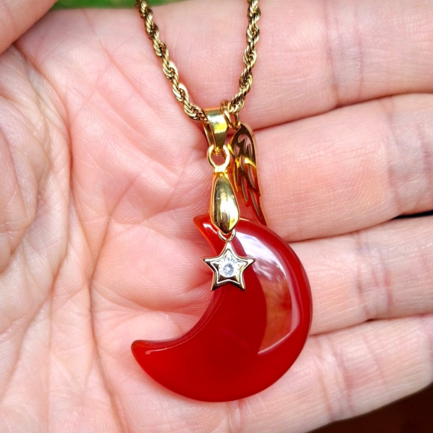 Collier lune en cornaline orange présenté dans la main avec breloques aile et étoile.
