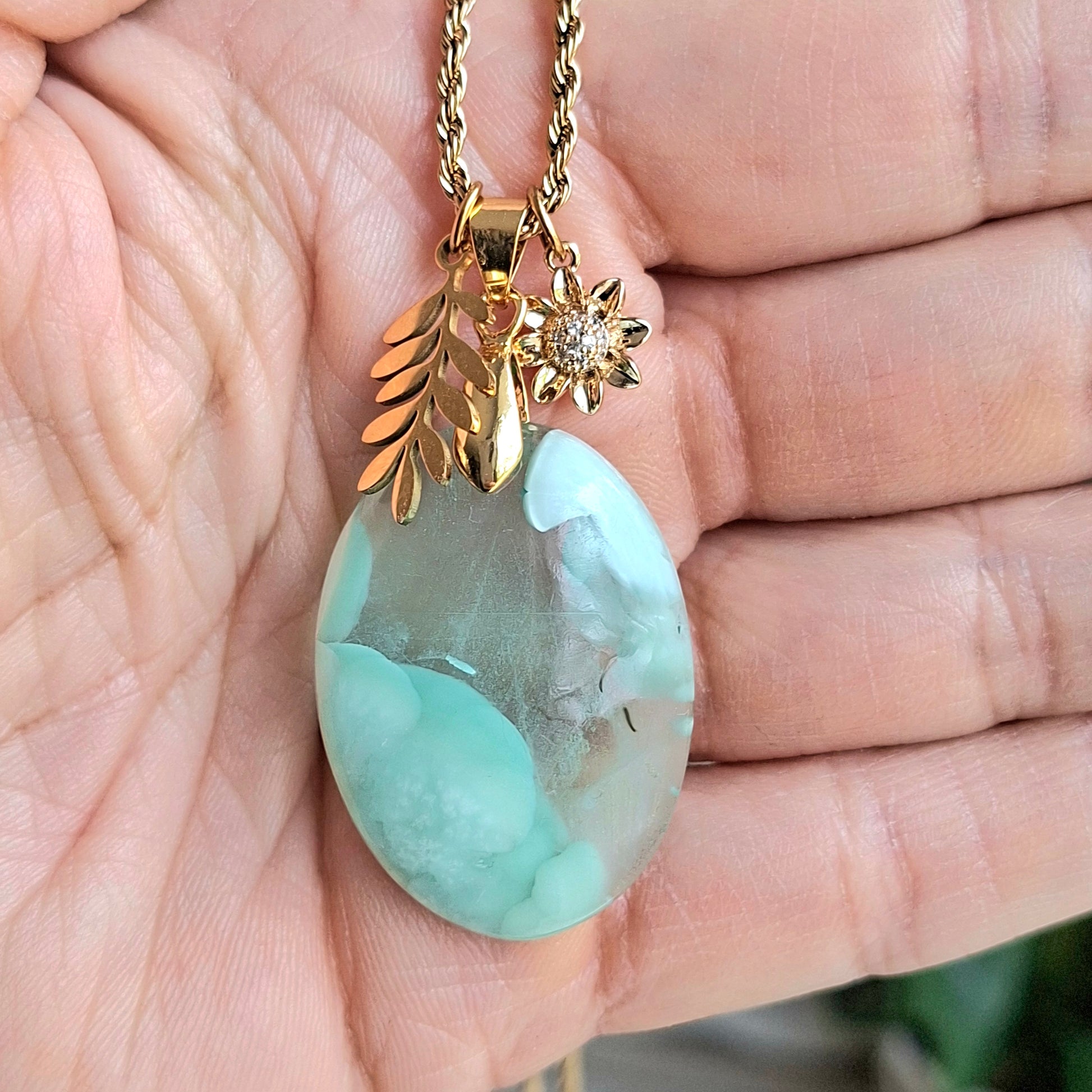 Collier hemimorphite ovale bleu pale pierre naturelle acier inoxydable dore feuille fleur zirconium dans la main