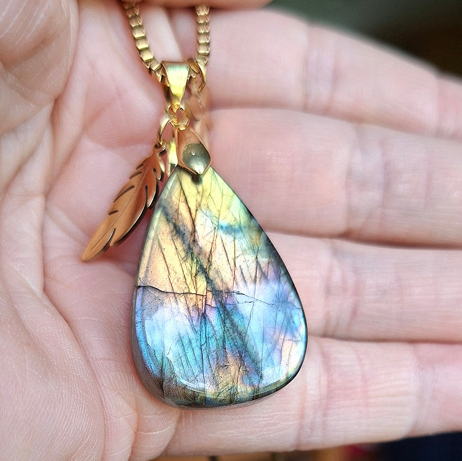 Collier en labradorite goutte présenté dans la main avec breloques plume et libellule dorées.