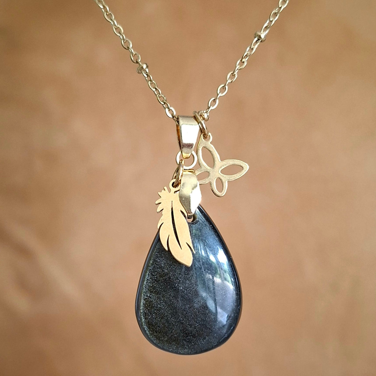 Collier en obsidienne dorée naturelle en forme de goutte avec papillon et plume dorés.
