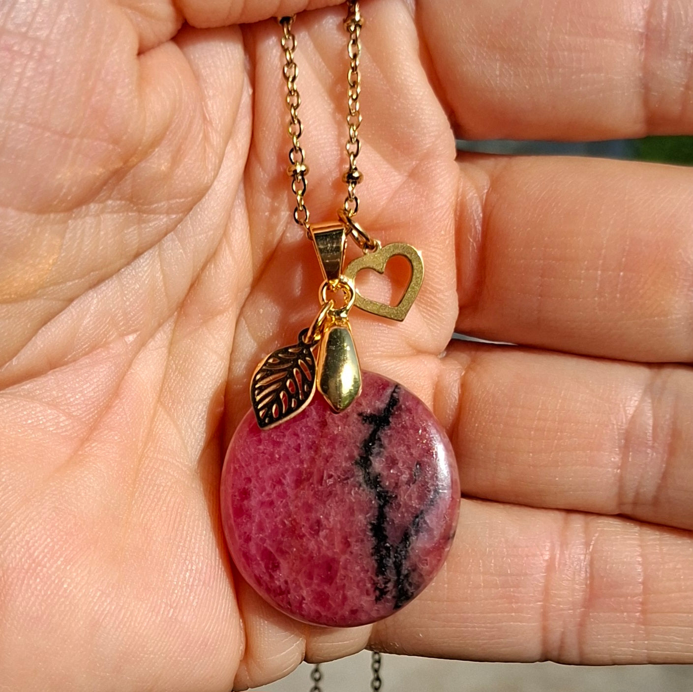 Pendentif rond en rhodonite naturelle rose et noire photographié en lumière naturelle