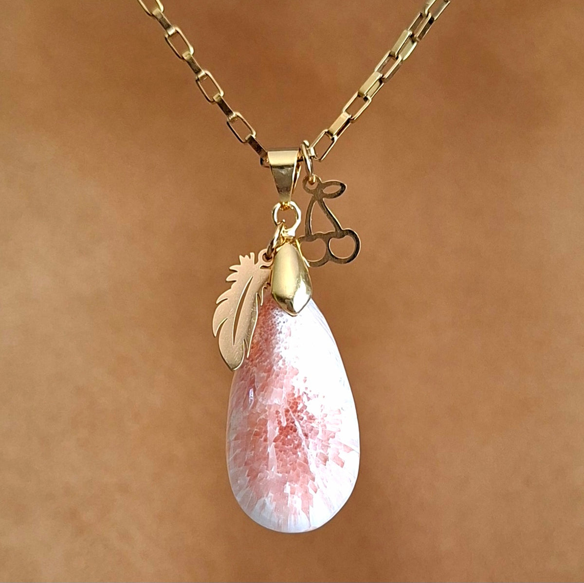 Collier en scolécite naturelle rose saumon et blanc nacré avec breloques plume et cerise dorées.