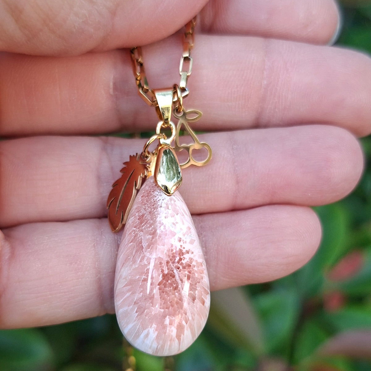 Collier en scolécite naturelle rose saumon aux reflets lumineux présenté dans la main.