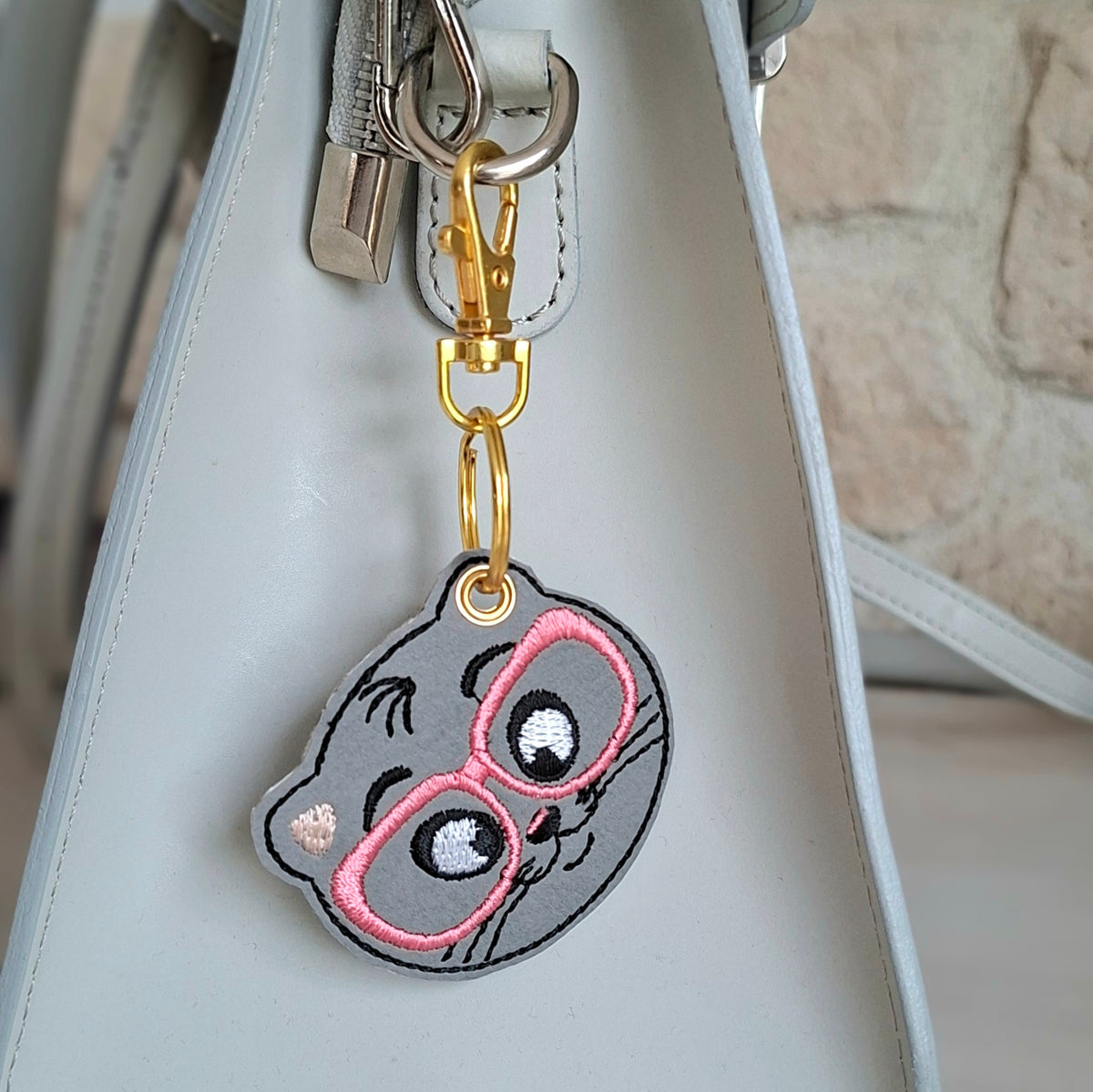 Chat brodé sur similicuir avec des lunettes roses accroché à un sac à main