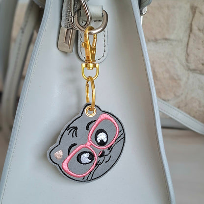 Chat brodé sur similicuir avec des lunettes roses accroché à un sac à main
